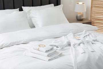Comfortable bed with clean linens, pillows, towels and bathrobe indoors