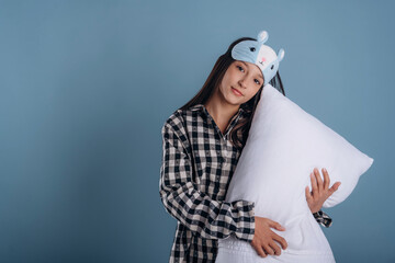 Big white pillow in hands. Young girl in pajama is against background