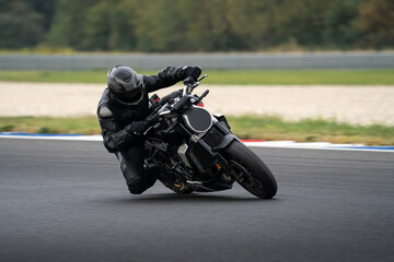 Motorcycle rider in a black leather suit riding fast on a black sport motorcycle through a corner...