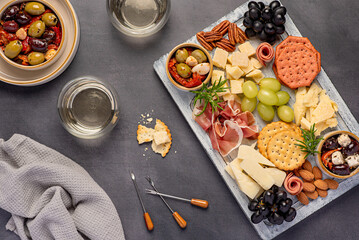 Food photography of white wine and antipasto with parmesan, sheep cheese, mature cheddar, serrano ham, prosciutto, grapes,  pecan; almond, crackers; marinated olives with dried tomatoes, party