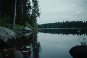 Obraz premium A tranquil lakeside view with smooth water reflecting the lush forest, set in a serene and isolated natural environment.