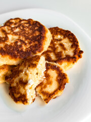 Golden syrniki on white plate with bite showing texture