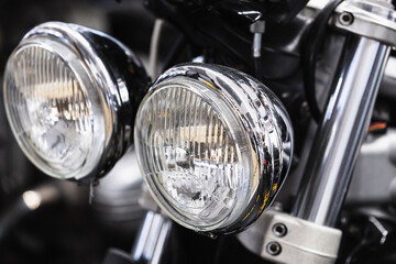 Round front headlights of a shiny black road motorcycle, close up