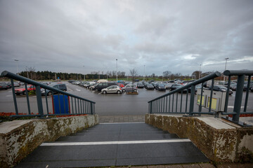Fototapeta premium Full parking lot, overcast day. Cars parked in rows, stairs leading down to the lot.