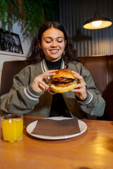 Happy customer about to eat a delicious hamburger with orange juice in a restaurant