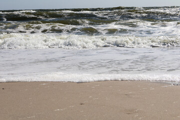 Gentle ocean waves meeting the sandy shoreline under bright sunlight, showcasing the beauty of a peaceful beach scene and the natural rhythm of the sea.