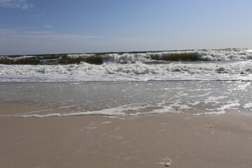 Sunny beach with gentle waves rolling onto the sandy shore under a clear blue sky, capturing a serene and tranquil coastal scene perfect for relaxation and nature themes.