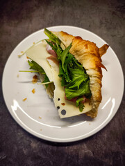 Delicious croissant sandwich with cheese and salad on white plate