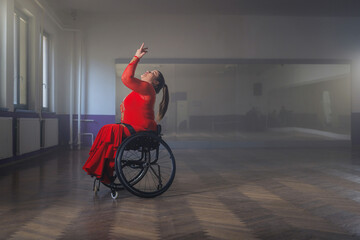 Woman in an elegant red dress dancing in a wheelchair, making graceful movements. Para dance sport concept.