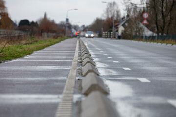 A wet, paved road with a bike lane separated by concrete barriers.  Residential buildings are...