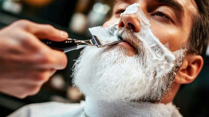 A barber applies shaving cream to a man's beard with a brush.