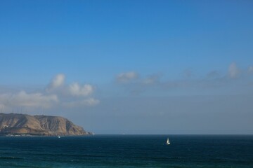 Serene coastal scene with sailboat and cliffs.