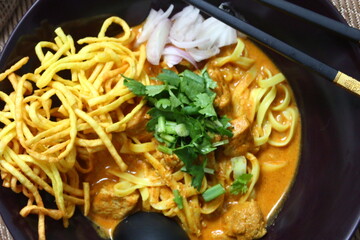 A bowl of Khao Soi, a Northern Thai noodle soup featuring egg noodles bathed in a fragrant coconut curry broth, topped with crispy noodles, pickled mustard greens, and fresh cilantro.