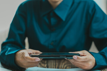 person holding smartphone while wearing blue shirt, focused on device. setting suggests modern and casual atmosphere, ideal for technology related content