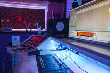 A music studio features a mixing console, computer, and ambient lighting. A soundproof booth with a...