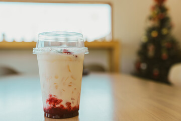 Creamy dessert in clear cup with red fruit topping, placed on wooden table. background features decorated tree, creating cozy atmosphere