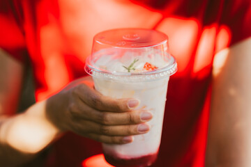 Refreshing beverage in clear cup held by person wearing red shirt. drink features layers of ice and...