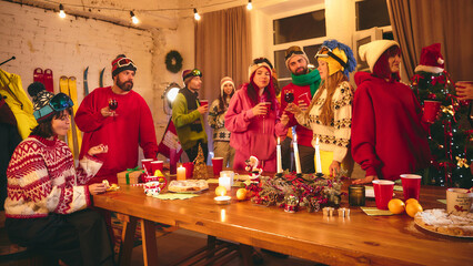 Holiday party scene with friends in ski-themed outfits enjoying festive drinks and snacks, surrounded by warm lighting, vintage skis, and glowing string lights Concept of holidays, Christmas party. Ad