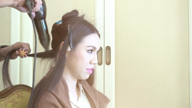 A woman with long hair is getting her hair done at a salon. She is wearing a brown sweater and has her hair in a ponytail