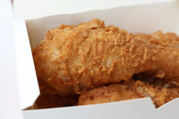 A box of fried chicken is sitting on a white table. The chicken is golden brown and crispy, and it looks delicious