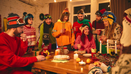 Holiday cheer abounds as friends in vibrant ski gear toast with red cups around candlelit table,...