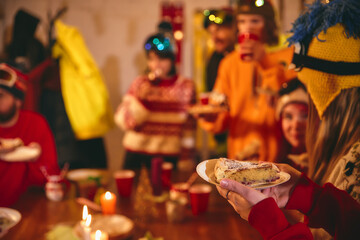 Joyful holiday party with friends in ski outfits gathered indoors, sharing laughter and toasting with red cups by decorated table filled with festive treats. Concept of holidays, Christmas party. Ad