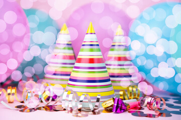 Multicolored striped party hats, balloons and decorations for party on pink background. Close-up.