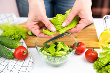 A young woman puts green lettuce leaves in a salad. The concept of healthy food. Close-up.