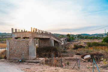 Abandoned Stone Bridge at Sunset in Rural Landscape with Overgrown Vegetation and Fencing, Highlighting Decay and History in Natural Surroundings Under a Clear Sky