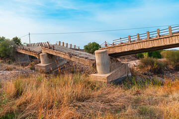 Abandoned Concrete Bridge in Rural Landscape Showing Signs of Destruction and Decay with Dry Vegetation and Clear Blue Sky