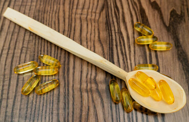 Wooden spoon rests on table with fish oil capsules scattered around