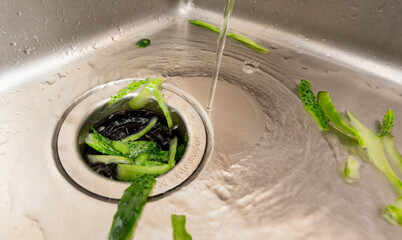 Efficient kitchen waste disposal system handling cucumber peels with running water in a modern sink setup.