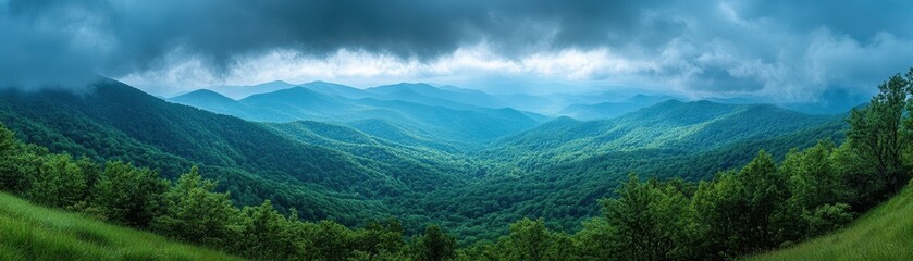 Obraz premium Majestic Mountain Range Under Dramatic Cloudy Sky with Lush Green Forests and Rolling Hills in a Serene Landscape