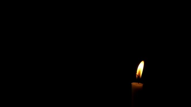 Close up of candle flame swaying in the wind isolated on black background.The candle flame is almost extinguished.The concept of hope and spirit.Copy space for text.Real time raw video no edit