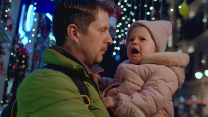 Man with crying daughter at street with Christmas lights and decoration, waiting for mother 