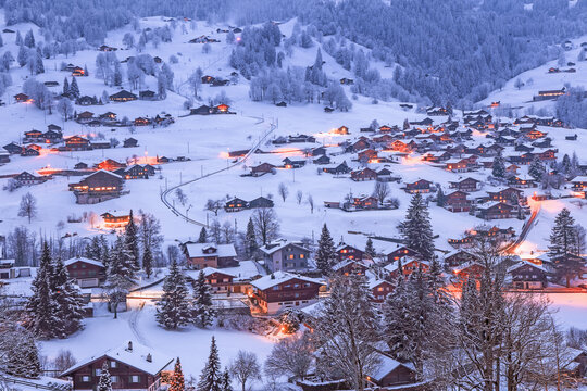 The famous dreamy slope of Grindelwald with wooden chalets covered with snow in cold winter season at twilight in Swiss Alps
