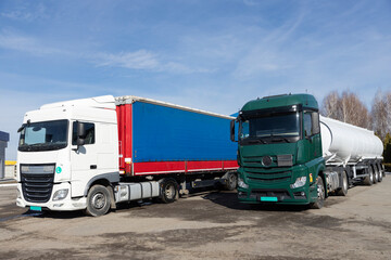 Two ten-wheeler trucks, one with a tank trailer, parked in the parking lot on a sunny day. Commercial vehicle for business transportation. Advertising of freight transport