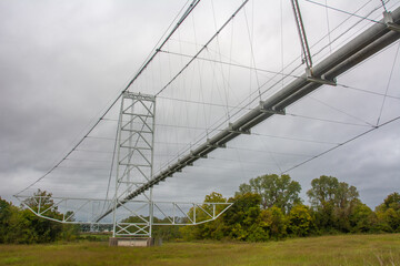 Fototapeta premium View of the single-span two-tower steel pipeline suspension bridge from underneath on a gloomy day with grey sky near Fulton, Arkansas, USA