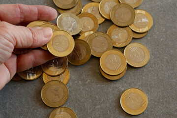 A close-up of a hand holding multiple gold coins, with more coins scattered on a flat surface. The image symbolizes wealth, savings, or monetary transactions..