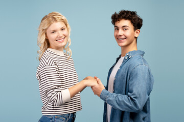 Happy, attractive young couple, smiling boy and girl wearing casual clothes holding hands each other