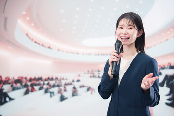 ホールで司会・プレゼンをするスーツを着た若い女性