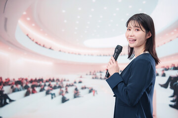 ホールで司会・プレゼンをするスーツを着た若い女性
