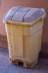Old orange plastic container for collecting household garbage with black wheels has suffered...