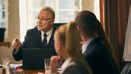 Senior businessman shares ideas and insights with colleagues during formal meeting, fostering teamwork and collaboration. Concept of business, leadership communication, vision, corporate meeting