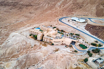 Aerial view of a multilevel building with modern architecture built on a hill at the foot of a mountain. Solitary residential area in Judean Desert, Israel. Picturesque landscape with hermitage.