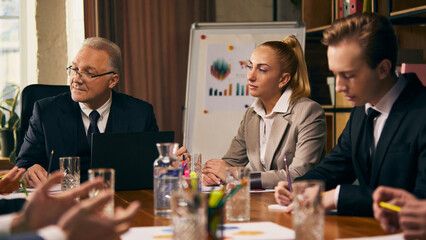 Group of business professionals in formal attire discussing charts and graphs during meeting in modern office setting. Analytics and strategy. Concept of business, teamwork, discussion, collaboration