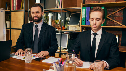 Two businessmen, colleagues in formal wear sitting at table during strategic business session, corporate meeting in modern office. Concept of business meeting, collaboration, brainstorming