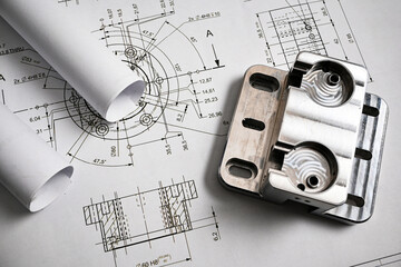 Metal part lying on engineering drawing with rolled blueprints, illustrating mechanical engineering...