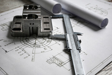 Metal machined parts lying on a technical drawing with a caliper, showcasing precision engineering and manufacturing