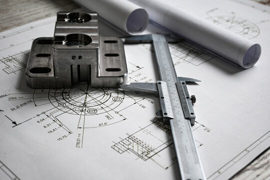 Metal machined parts lying on a technical drawing with a caliper, showcasing precision engineering and manufacturing